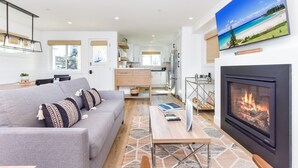 Una sala de estar moderna con un sofá gris, una chimenea y una pantalla grande mostrando una escena de playa.