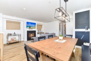 A modern living room with a fireplace, a dining table, and a large window with a view of the beach. - BRAND NEW Luxury 1 Bedroom Condo Steps from the Beach (Newport Beach)