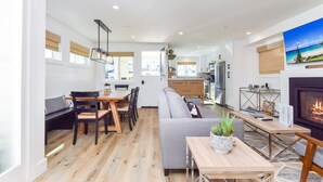 Una sala de estar moderna con un sofá, mesa de comedor y sillas. Se observa una chimenea y una cocina al fondo.