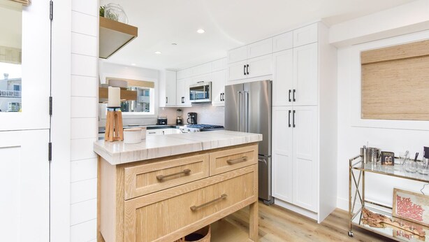 Una cocina moderna con armarios blancos, encimera de madera y electrodomésticos de acero inoxidable.