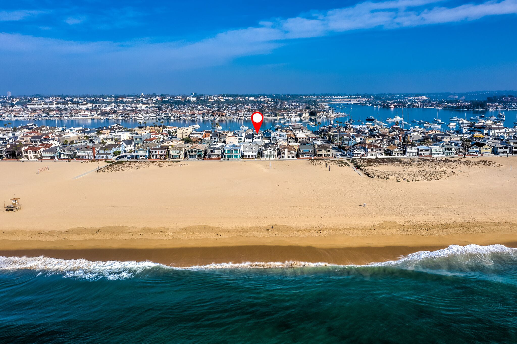 An aerial view of a coastal town with a beach, marina, and dense residential area.