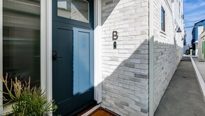 Un edificio moderno con una puerta azul, fachada de ladrillo blanco y un letrero con la letra 'B' que indica el nombre del edificio.