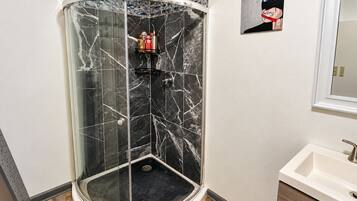 A glass-enclosed shower with a marble wall, a sink, and a framed picture on the wall.