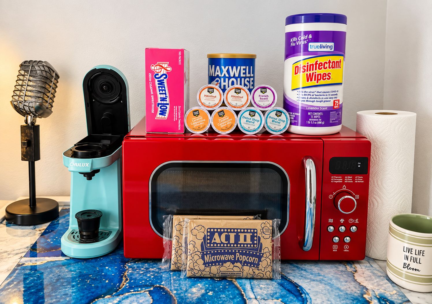 A microwave oven with a popcorn box, a microphone, a box of Sweet'N Low, a can of Maxwell House coffee, a container of disinfectant wipes, and a roll of paper towels.