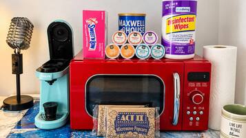A microwave oven with a popcorn box, a microphone, a box of Sweet'N Low, a can of Maxwell House coffee, a container of disinfectant wipes, and a roll of paper towels.