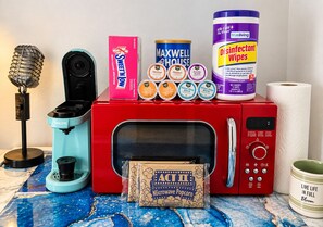 A microwave oven with a popcorn box, a microphone, a box of Sweet'N Low, a can of Maxwell House coffee, a container of disinfectant wipes, and a roll of paper towels. - The Cozy King Studio #1 (Benton)