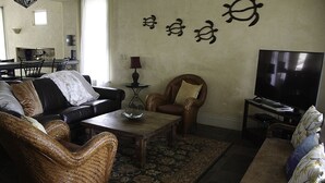 A living room with a sofa, armchairs, a coffee table, a TV, and a wall with decorative elements.