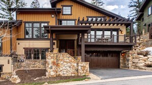 Une maison moderne à deux étages, avec des fondations en pierre, un revêtement extérieur en bois et un balcon agrémenté de mobilier d’extérieur.