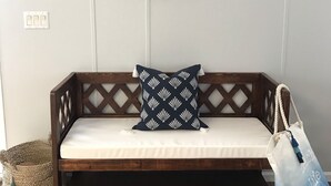 A wooden bench with a white cushion, a patterned pillow, and a hat hanging on the wall.
