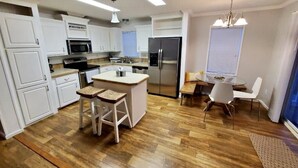 A modern kitchen with white cabinetry, a stainless steel refrigerator, and a central island with stools.