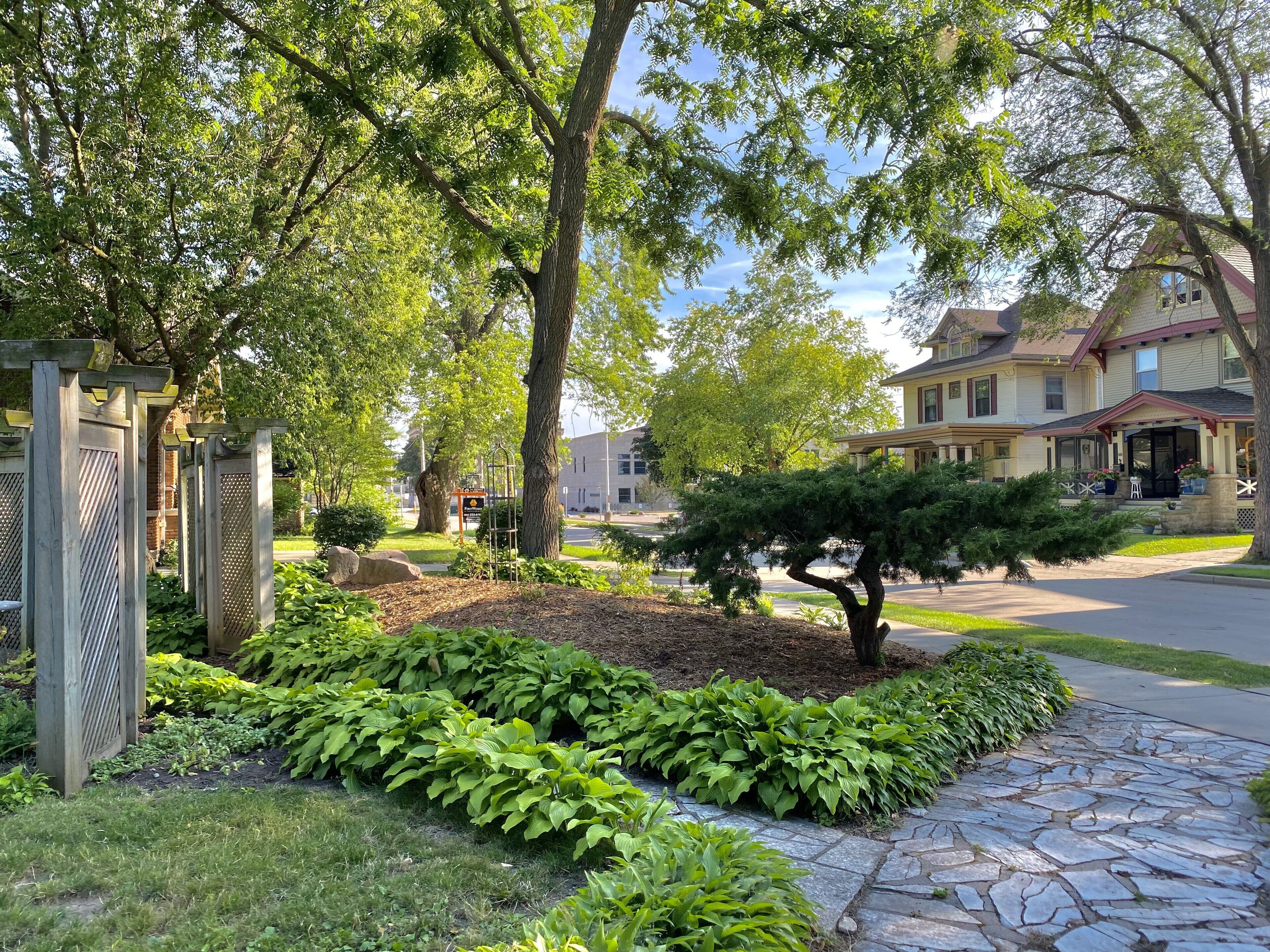 Une rue résidentielle bordée de jardins bien entretenus, d’un chemin de pierre et de maisons dotées de vérandas.