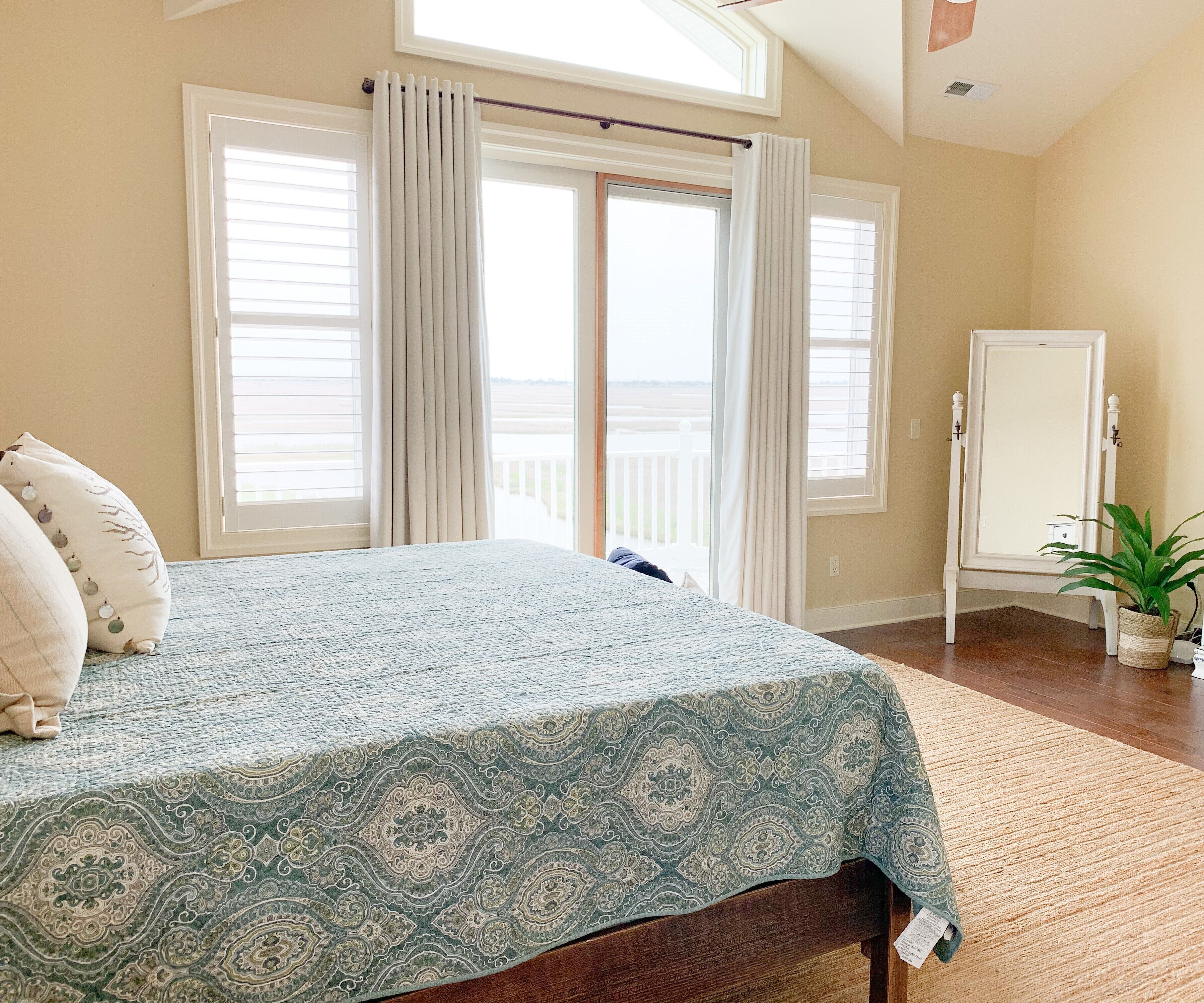 A bedroom with a bed, a nightstand, a potted plant, and a view of the outdoors through a window.