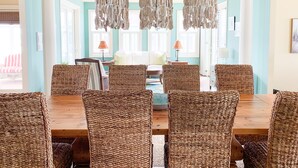 Comedor con mesa de madera y sillas de mimbre, lámpara colgante y vista del salón contiguo.