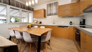A modern kitchen with wooden cabinets, a white countertop, and a dining area with a wooden table and white chairs. - Villa Alexandros luxury achillion corfu  (Corfu)