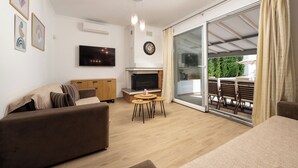 A modern living room with a sofa, a TV, a fireplace, and a sliding glass door leading to an outdoor area. - Villa Alexandros luxury achillion corfu  (Corfu)