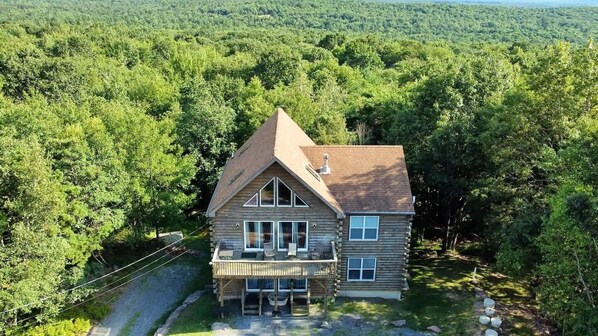 A log cabin with a balcony, surrounded by dense forest. - Secluded Retreat w Beach/Lake Access: Hot Tub, BBQ, Sleeps 16 (Blakeslee)