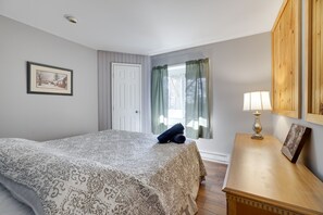 A bedroom with a bed, a nightstand, a lamp, a framed picture, a door, and a window with curtains. - Secluded Retreat w Beach/Lake Access: Hot Tub, BBQ, Sleeps 16 (Blakeslee)