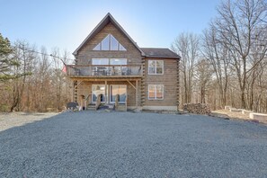 A two-story log cabin with a balcony, a front porch, and a gravel driveway. - Secluded Retreat w Beach/Lake Access: Hot Tub, BBQ, Sleeps 16 (Blakeslee)
