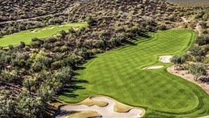 Siisti ja hyvin hoidettu golfkenttä, jossa on tasaiset väylät, hiekkabunkerit ja kirkas taivas.