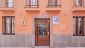 Fachada de edificio con puerta de madera, ventanas con rejas y un cartel que indica un complejo de apartamentos.
