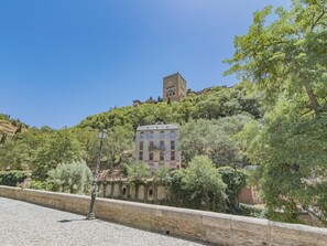 Edifici històric amb una torre, envoltat de vegetació exuberant i una paret de pedra.