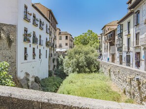 Un carrer estret amb edificis a ambdós costats, una paret de pedra i verdura al mig.