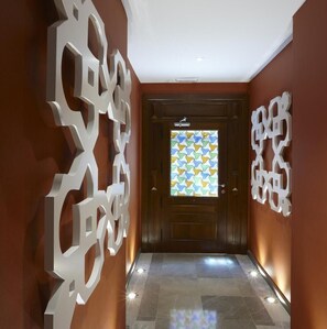 Stylish hallway with a geometric patterned window, abstract art, and neutral tile flooring.