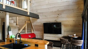 A wooden interior with a kitchen area, a dining table with chairs, and a TV mounted on the wall. - Picturesque Mountain Views, Direct Snowmobile & ATV trail access. 30 minutes to Sunday River and Black Mountain of Maine. (Andover)