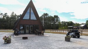 A triangular building with a large glass window, a gravel driveway, and a golf cart parked nearby. - Picturesque Mountain Views, Direct Snowmobile & ATV trail access. 30 minutes to Sunday River and Black Mountain of Maine. (Andover)