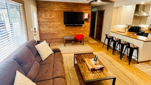 A modern living room with a brown sofa, a coffee table, and a TV mounted on a wooden wall.