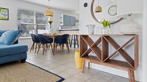 Een moderne woonkamer met een blauwe bank, een eethoek met stoelen, een houten console tafel en een keuken op de achtergrond.