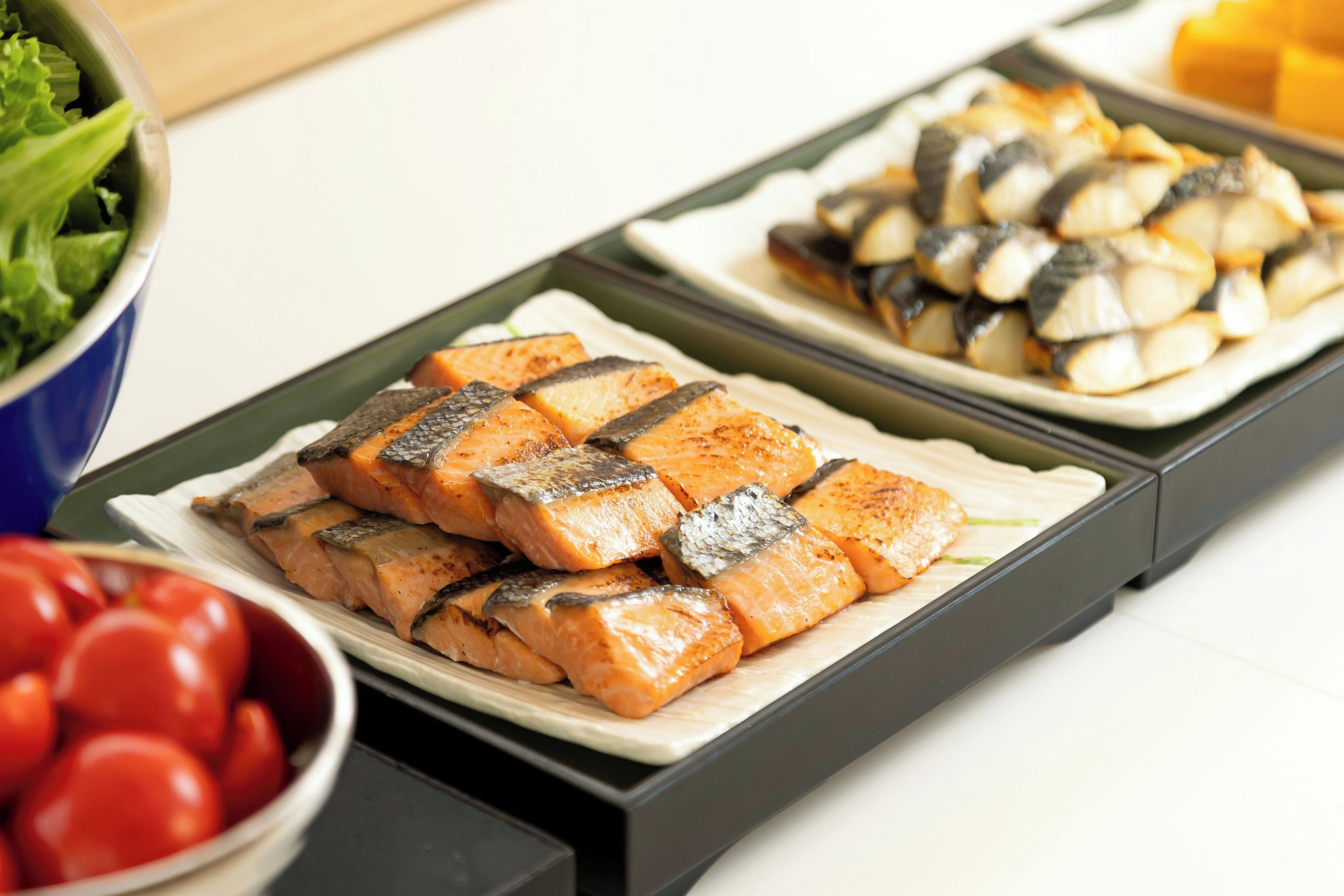 A buffet with various dishes including salmon, eggs, and tomatoes.