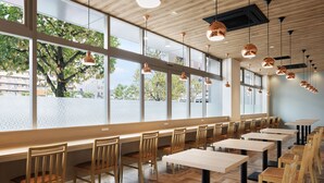 Ein modernes Restaurant mit langen Holztischen und -stühlen, großen Fenstern und hängenden Kupferlampen.