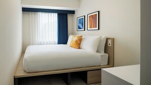 Ein Hotelzimmer mit einem Bett, einem Nachttisch, einem Fenster mit Vorhängen und zwei gerahmten Bildern an der Wand.