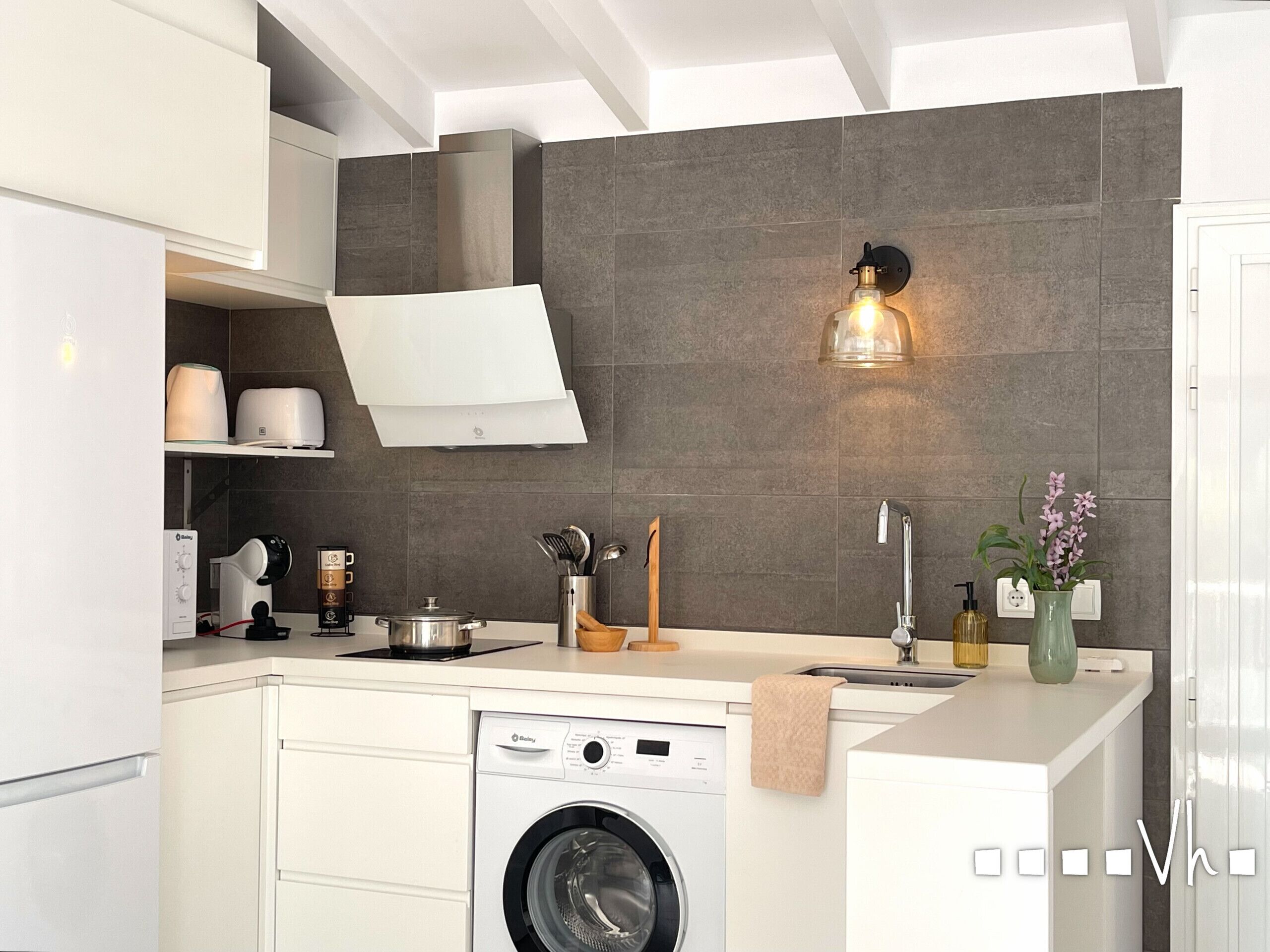 A modern kitchen with a built-in washing machine, a coffee machine, and a wall-mounted light fixture.