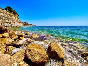 A rocky shoreline with clear blue water and a cliff with vegetation.