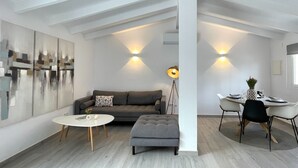 Una sala moderna con sofá, reposapiés y una mesa de centro, un comedor con sillas y una mesa, y un cuadro abstracto grande en la pared.