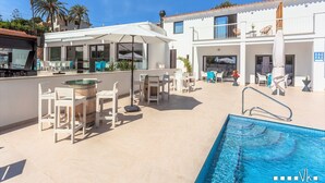 Un área de piscina moderna al aire libre con bar, asientos y un porche cubierto.