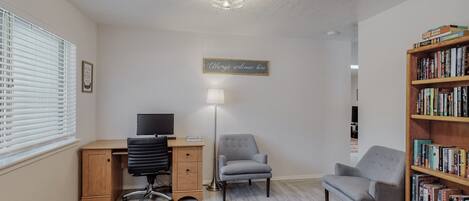 A home office with a desk, two chairs, a bookshelf, and a "Always welcome here" sign.