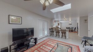 A modern living room with a flat-screen TV, a ceiling fan, and a dining area with bar stools. - NEW Renovated Private 3/2Home(King)Near Balloon Fiesta Park, Quiet Neighborhood! (Albuquerque)