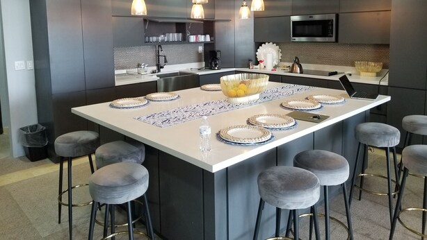 A modern kitchen with a central island, bar stools, pendant lights, and a microwave.