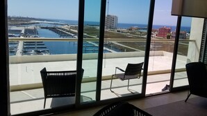 A room with large windows overlooking a marina and the ocean. There are two chairs and a small table in the room.