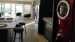 A modern kitchen with a built-in washer and dryer, a large island with bar stools, and a view through large windows.