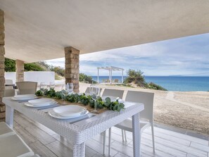 Un espace extérieur aménagé pour les repas, avec une table dressée pour quatre personnes, donnant sur une plage.