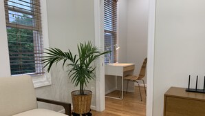 Una habitación con suelo de madera, un escritorio blanco con silla, una planta en maceta y una lámpara.