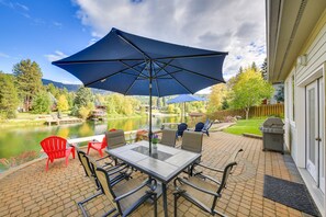 En terrasse med et bord og stole, en stor parasol og udsigt til en sø og bjerge.