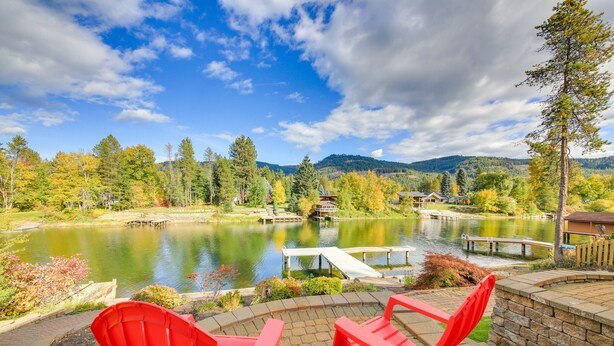 A patio with red Adirondack chairs overlooking a lake, surrounded by trees and a mountain in the background. - Expansive Waterfront Escape w/ Kayaks + SUPs! (Sagle)