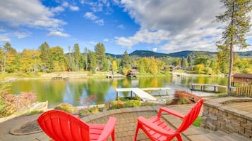 Une terrasse avec des fauteuils Adirondack rouges donnant sur un lac, entourée d’arbres et avec une montagne en arrière-plan.