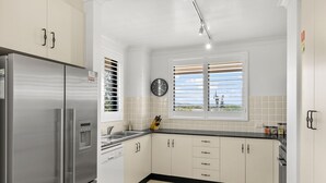 A modern kitchen with white cabinets, stainless steel appliances, a built-in oven, and a window with blinds. - Byron Breeze 7 ~ Luxury Penthouse 3 Bedroom Apartment (Byron Bay)