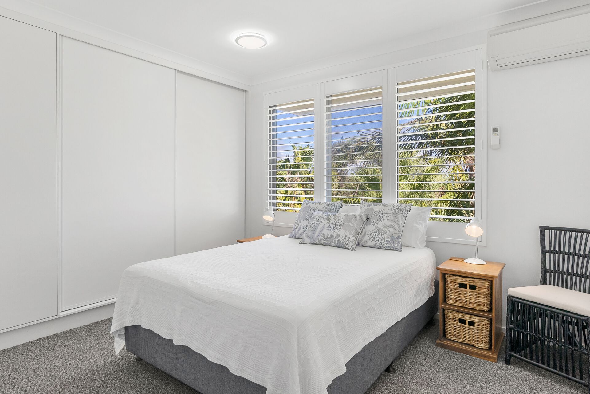 A bedroom with a bed, a nightstand, a chair, and a window with blinds.